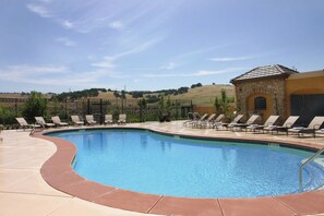A swimming pool with lounge chairs and a stone building in the background. - Holiday Inn Express & Suites El Dorado Hills by IHG (El Dorado Hills)