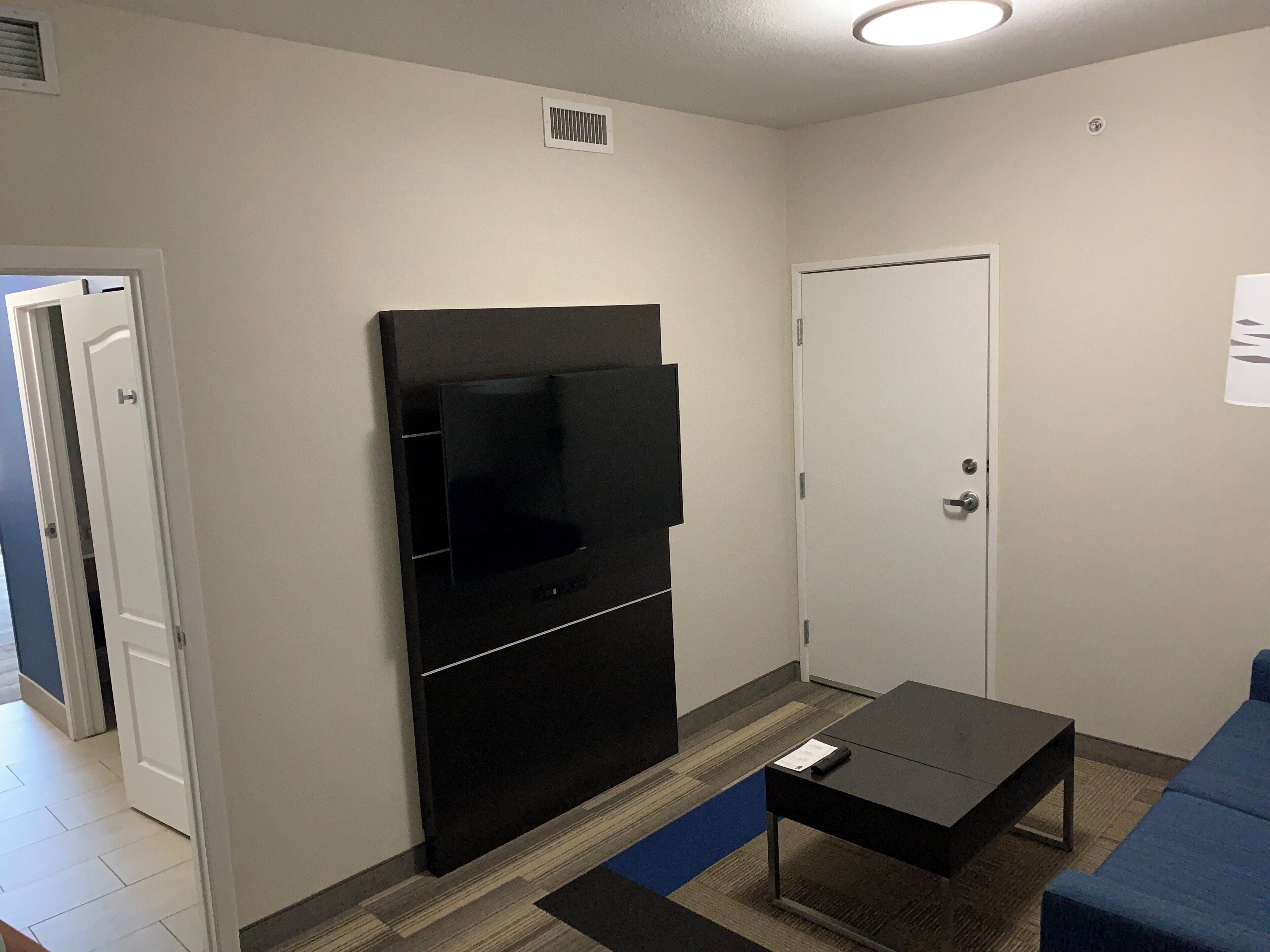 A room with a flat-screen TV mounted on the wall, a small table, a blue couch, and a door.