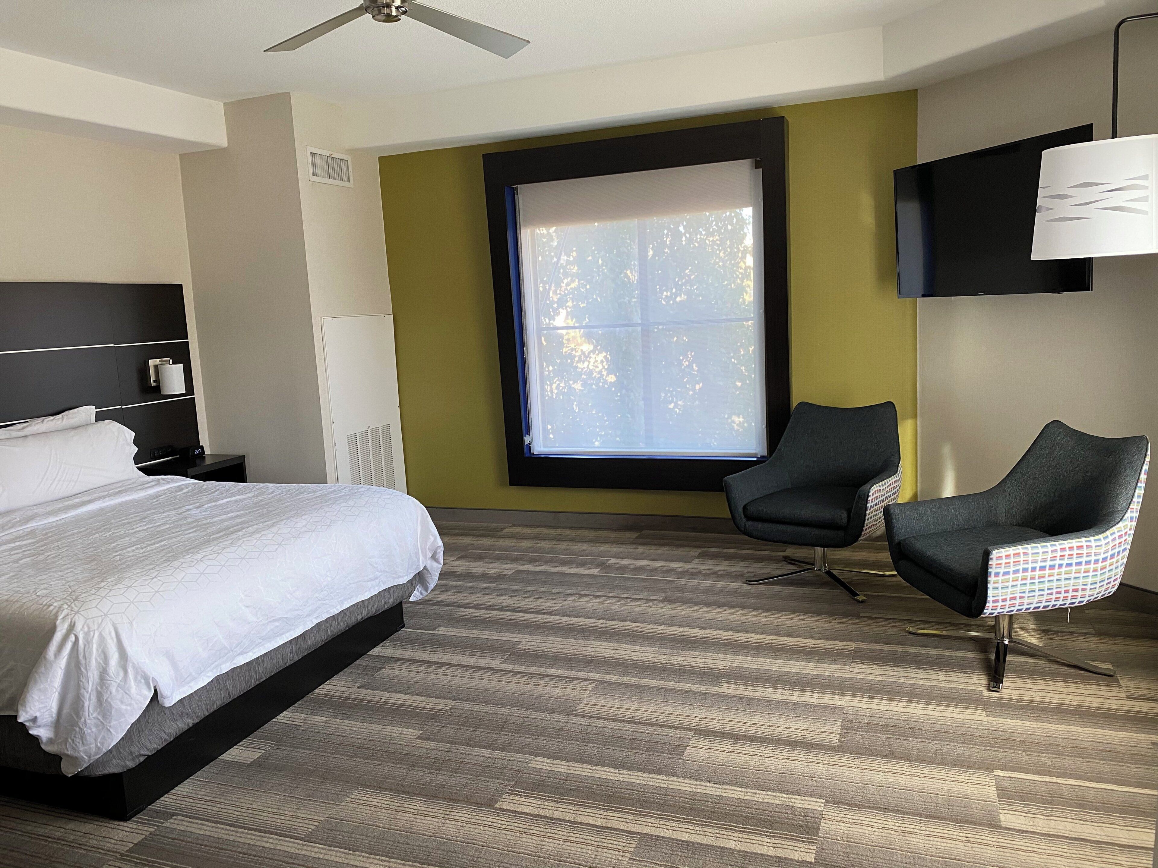 A hotel room with a bed, a chair, a TV, and a window.