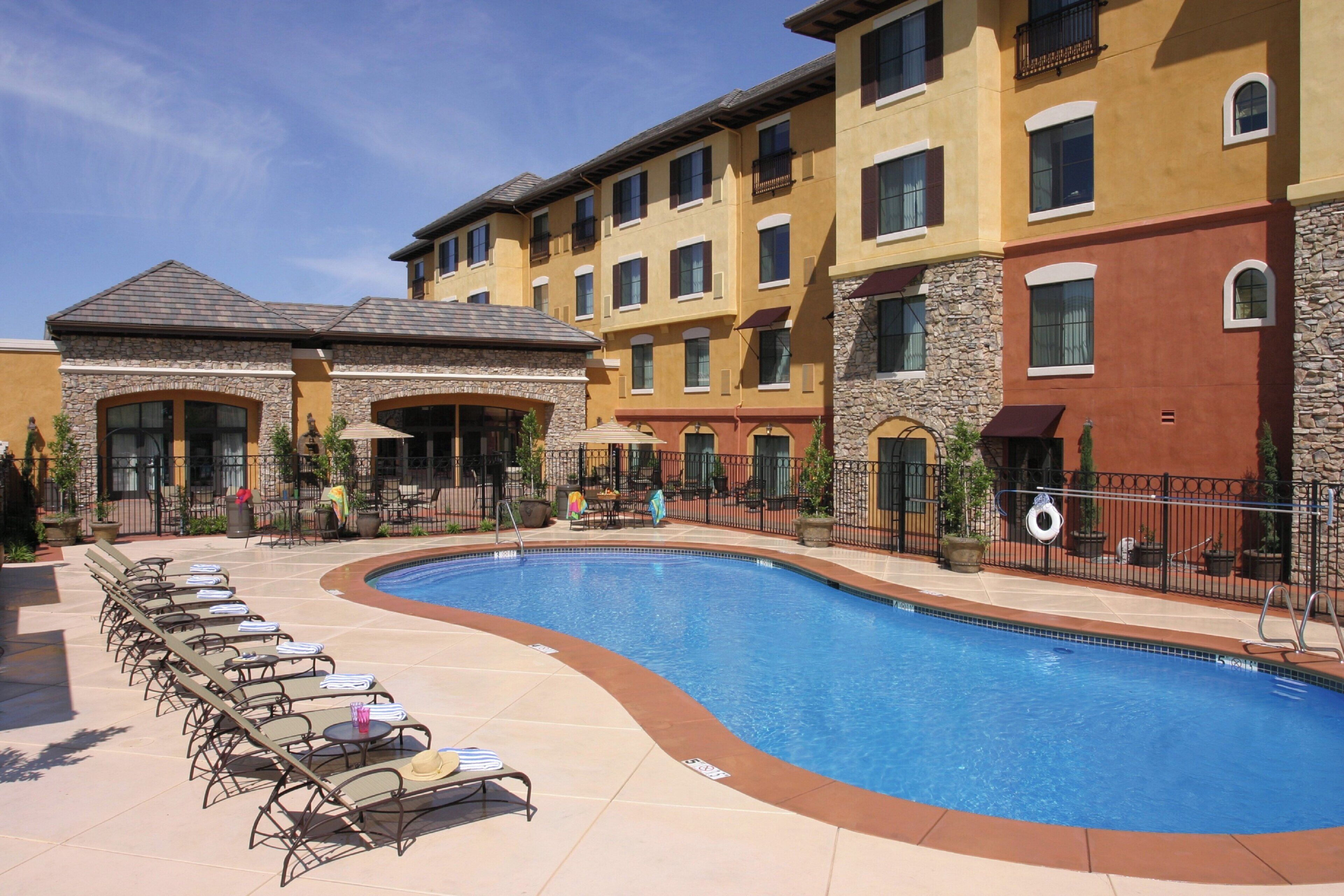 A hotel with a swimming pool, lounge chairs, and a stone facade.