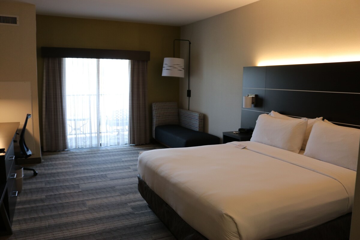 Een hotelkamer met een groot bed, een bureau met stoel, een televisie en een raam met gordijnen.