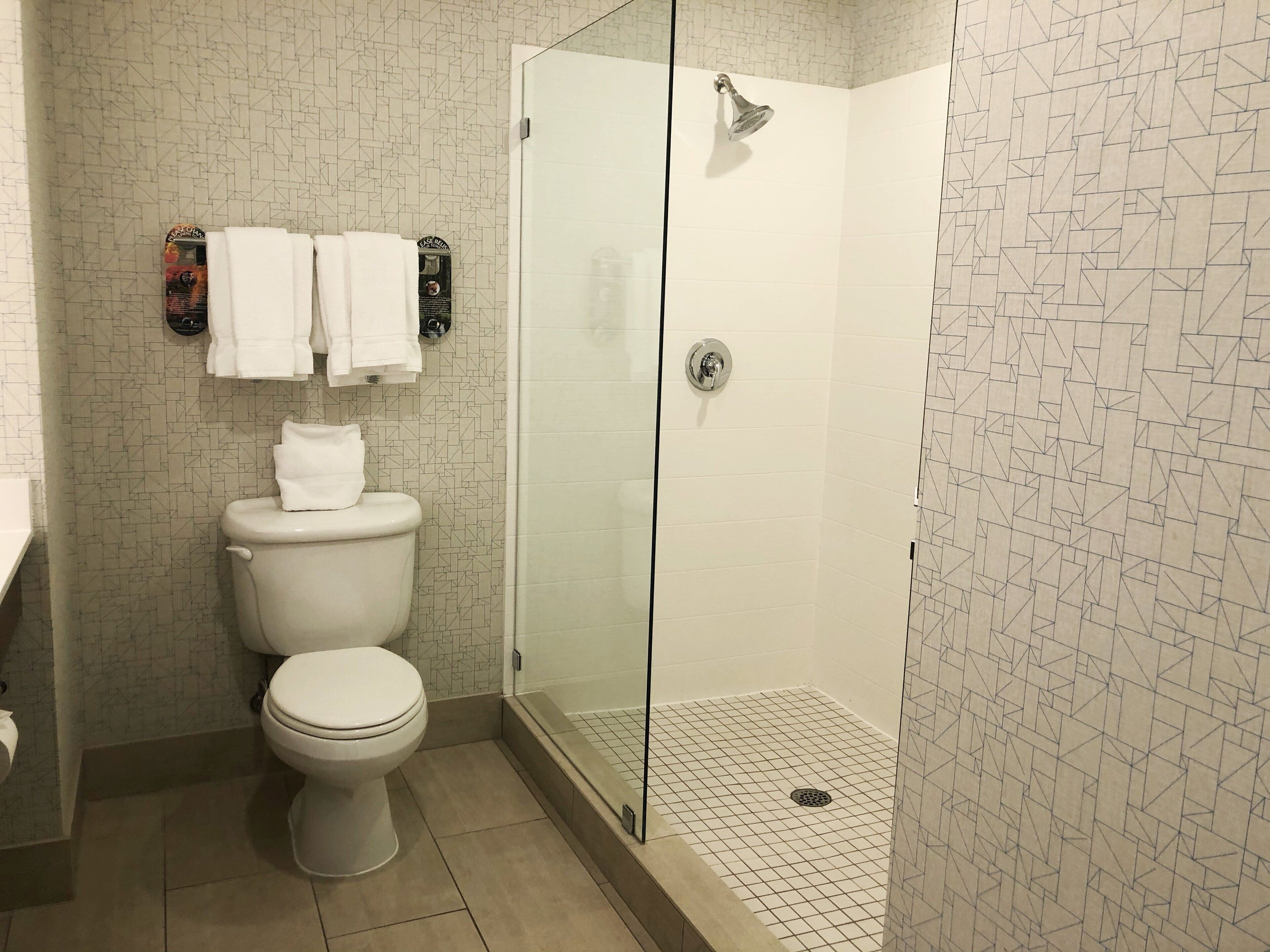 Een badkamer met toilet, douche met glazen deur en een behang met patroon.