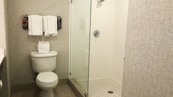 A bathroom with a toilet, a shower with a glass door, and a patterned wall.
