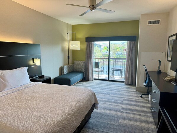 Une chambre d’hôtel avec un grand lit, un bureau avec un ordinateur, une chaise, une petite table et un balcon donnant sur l’extérieur.