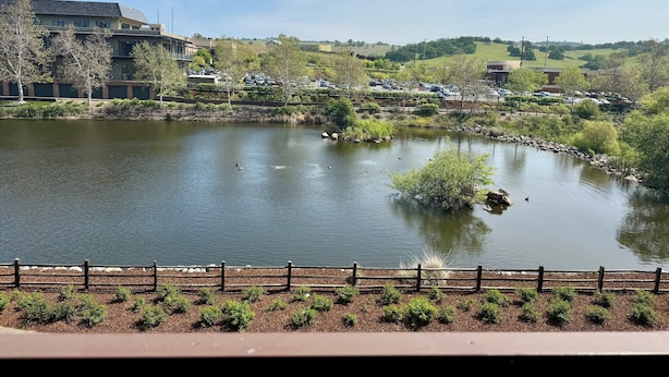 A lake with a wooden fence in the foreground, surrounded by greenery and buildings in the background. - Holiday Inn Express & Suites El Dorado Hills by IHG (El Dorado Hills)