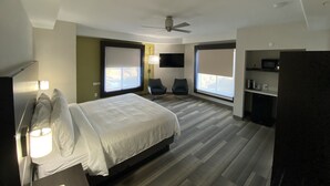 Een moderne hotelkamer met een groot bed, twee stoelen, een televisie en een plafondventilator.
