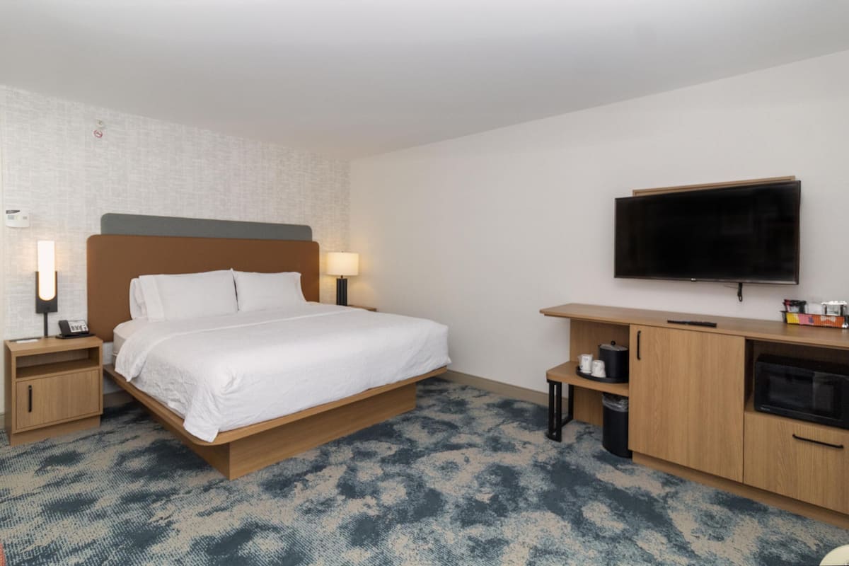A hotel room with a bed, bedside lamps, a TV, a wooden desk, and a trash bin.