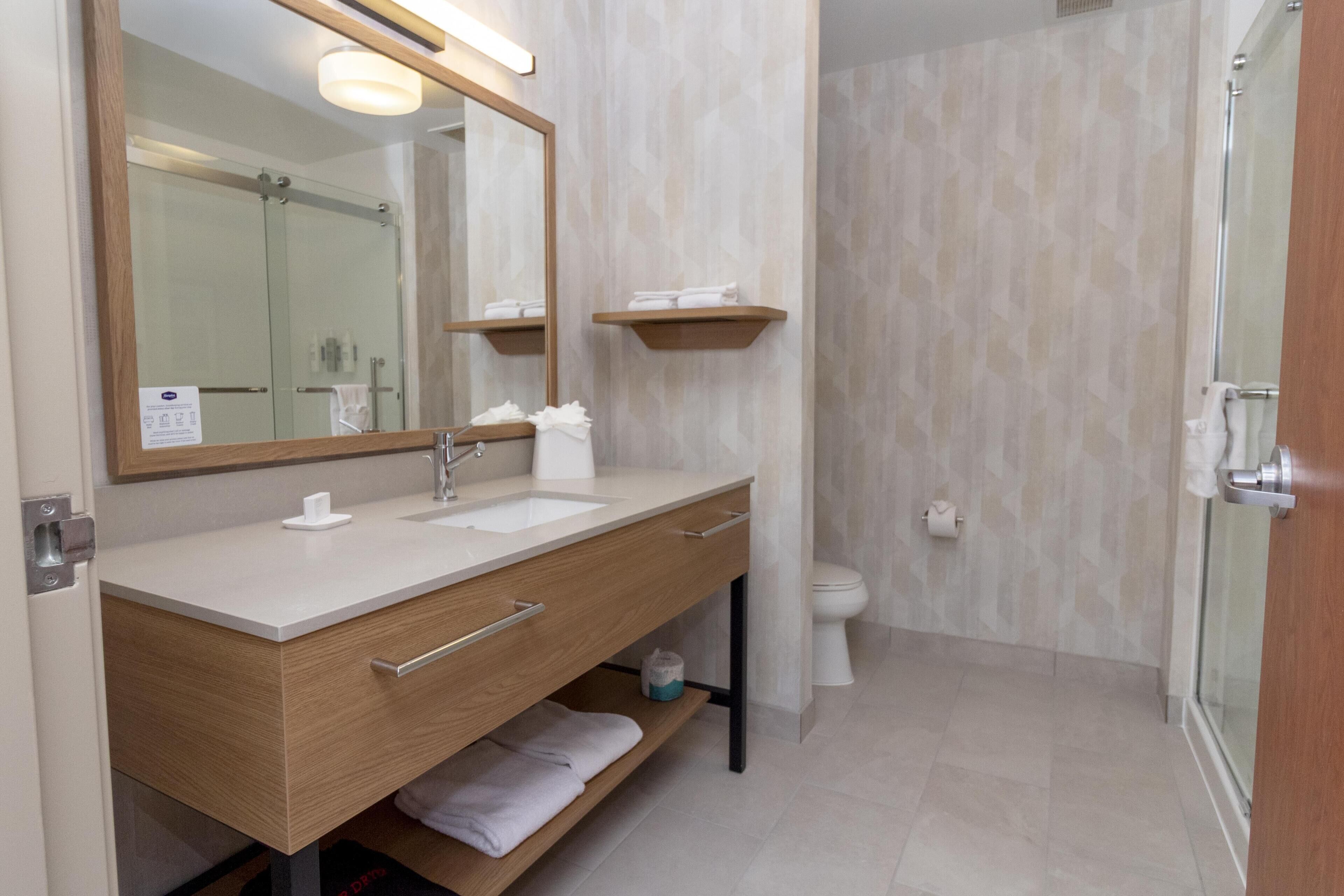 A modern bathroom with a wooden vanity, a large mirror, a sink, a toilet, and a glass shower enclosure.