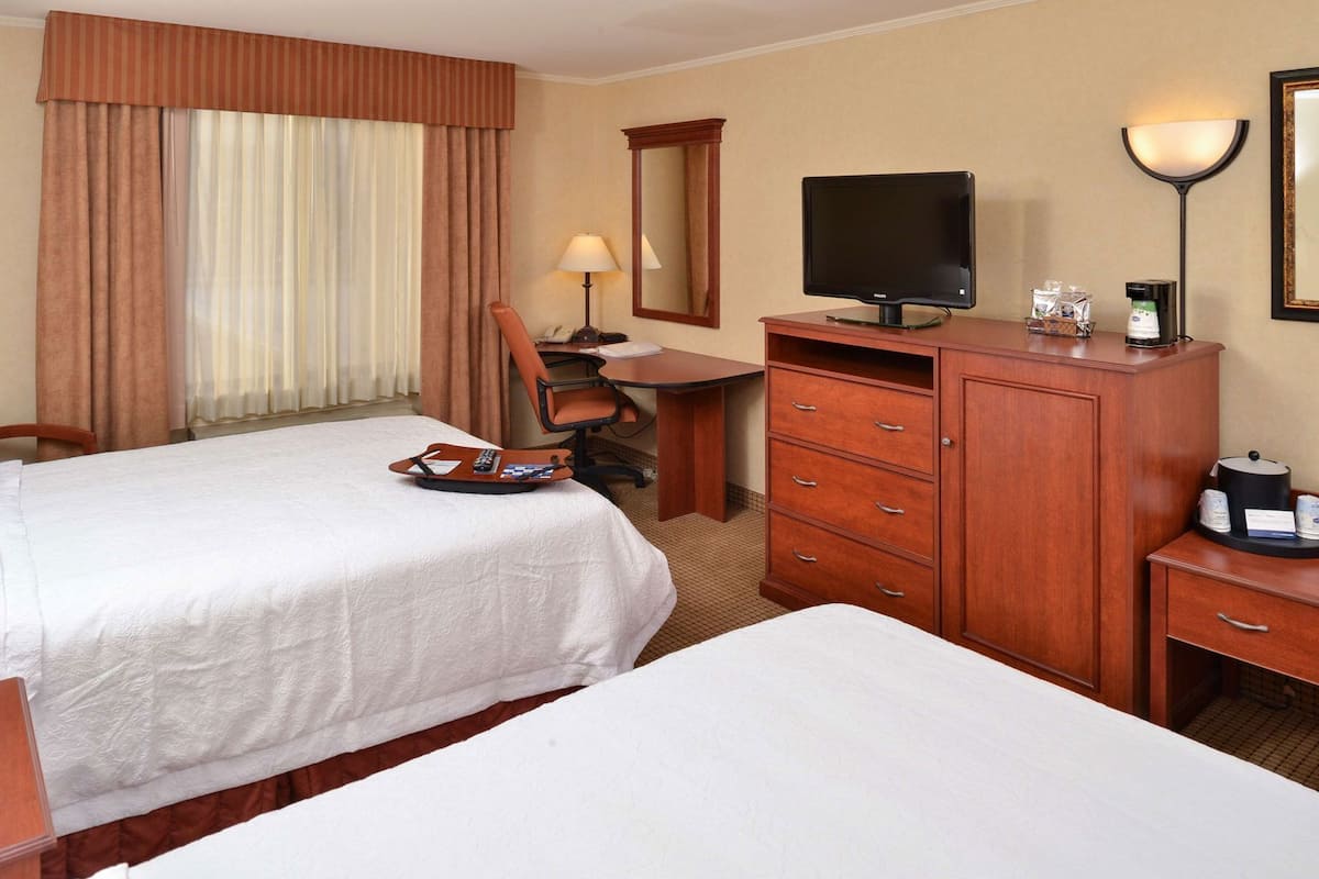 A hotel room with two beds, a desk with a computer, a chair, a dresser, and a TV.