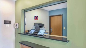 Un comptoir d’accueil avec une cloison en verre, un guichet d’enregistrement, un espace d’accueil avec un mur bleu, une porte et un panneau indiquant le numéro 6.
