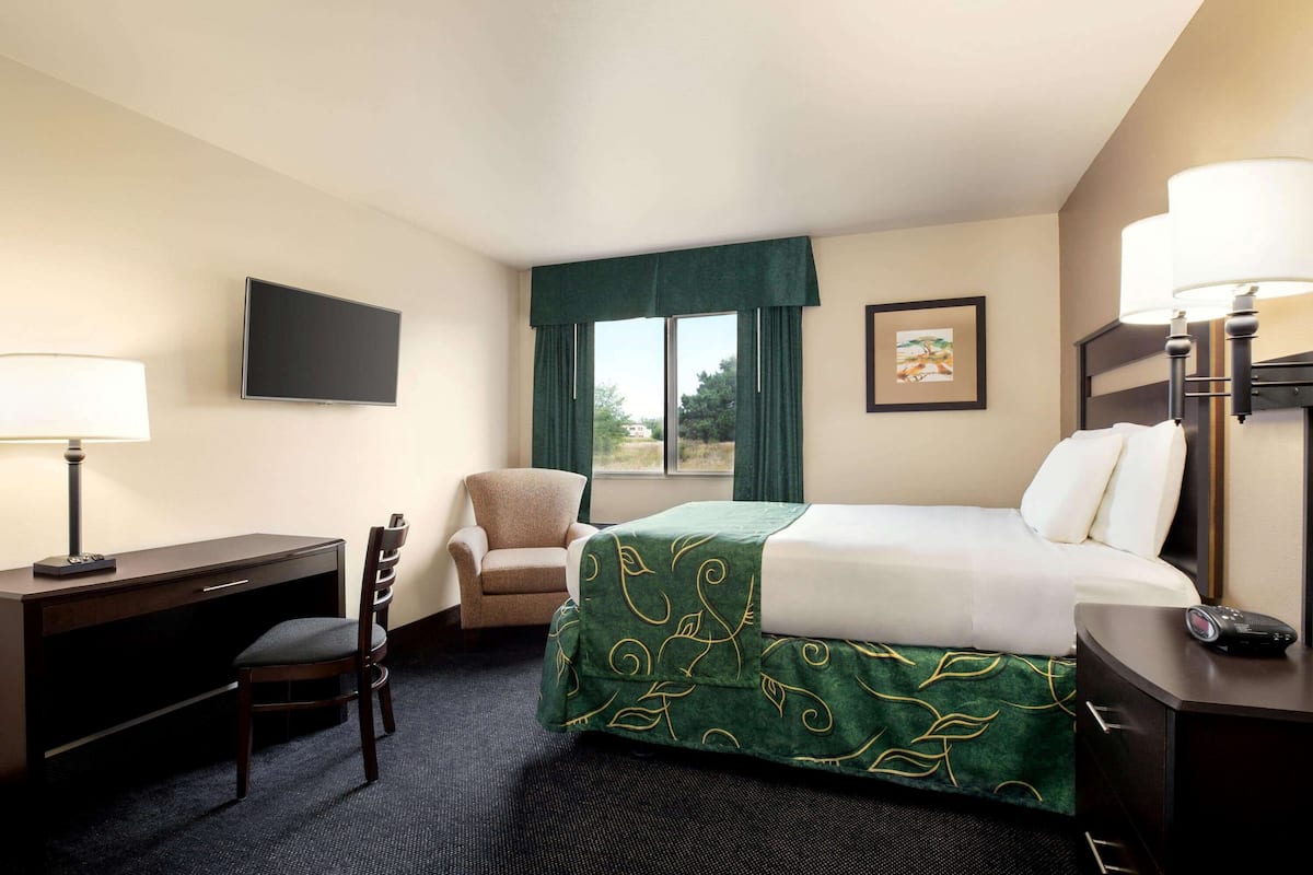 A hotel room with a bed, desk, chair, TV, and window with curtains.