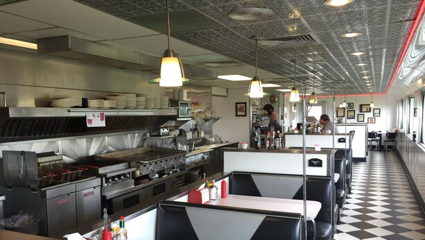 Un restaurante con mesas tipo cabina, zona de cocina y suelo a cuadros.