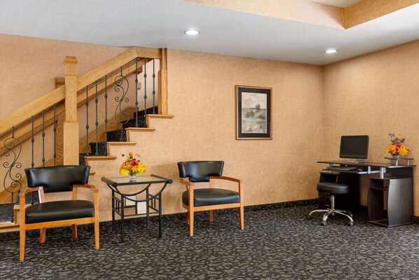 A hotel lobby with a staircase, two chairs, a small table with a vase, and a desk with a computer.