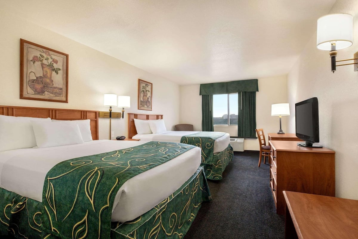 A hotel room with two beds, a desk, a television, and artwork on the walls.