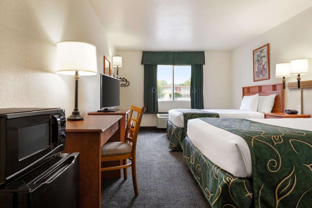 A hotel room with a desk, television, two beds, a chair, and a window with curtains.