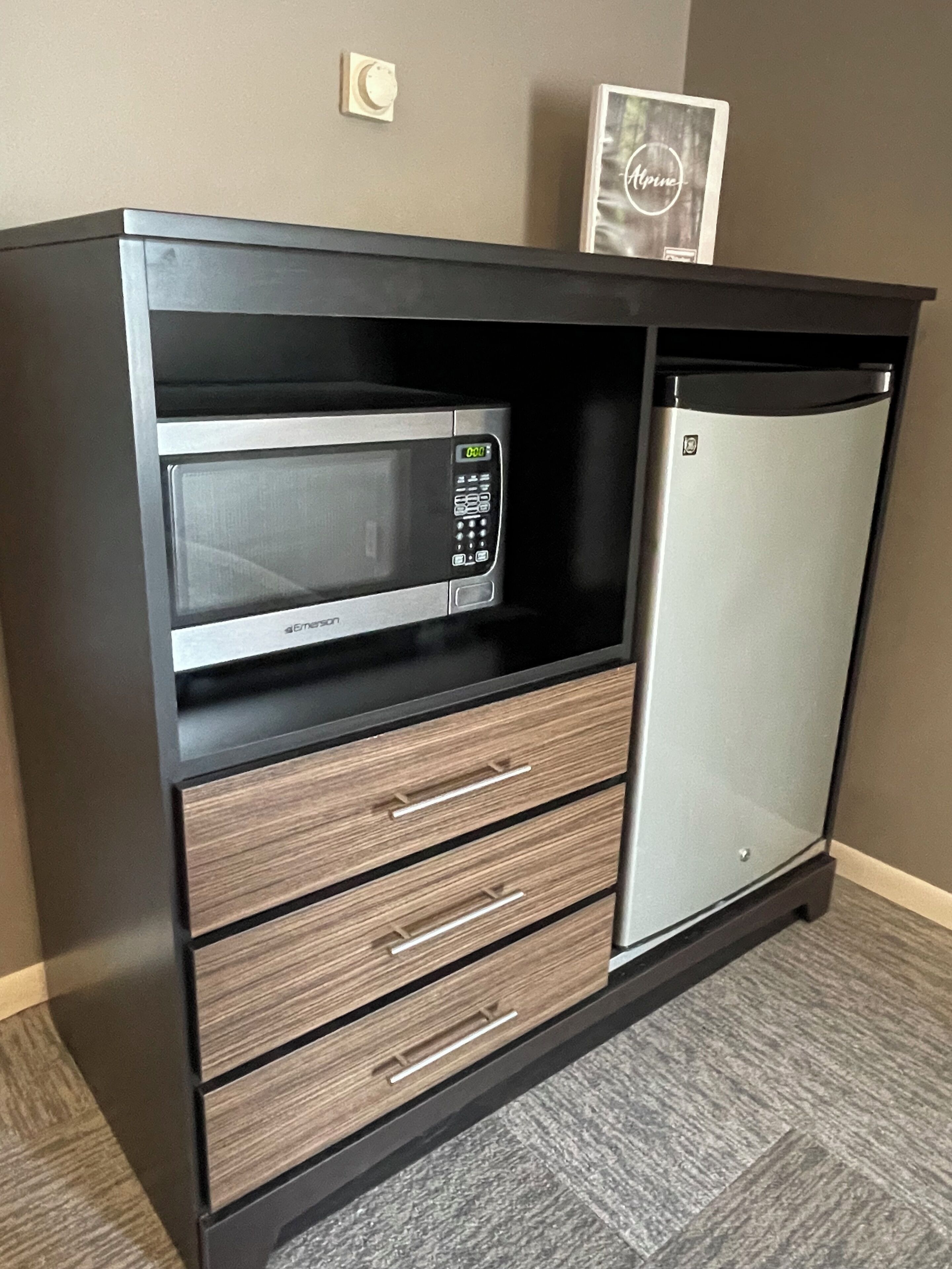A kitchenette with a microwave, a refrigerator, and wooden drawers.