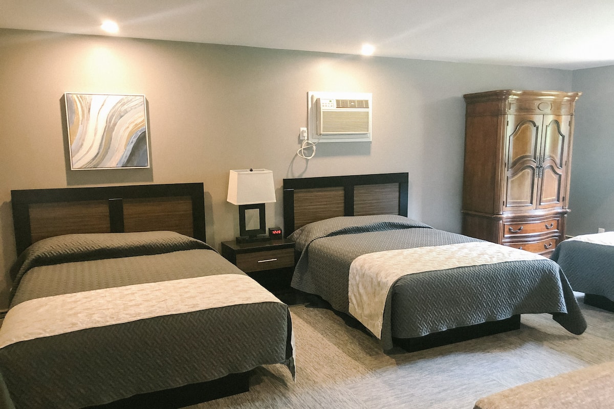 A hotel room with two beds, a nightstand with a lamp, a wardrobe, and a painting on the wall.