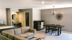 Una sala moderna con un sofá modular, una mesa de comedor con sillas, una pequeña mesa de centro, un microondas y un refrigerador.