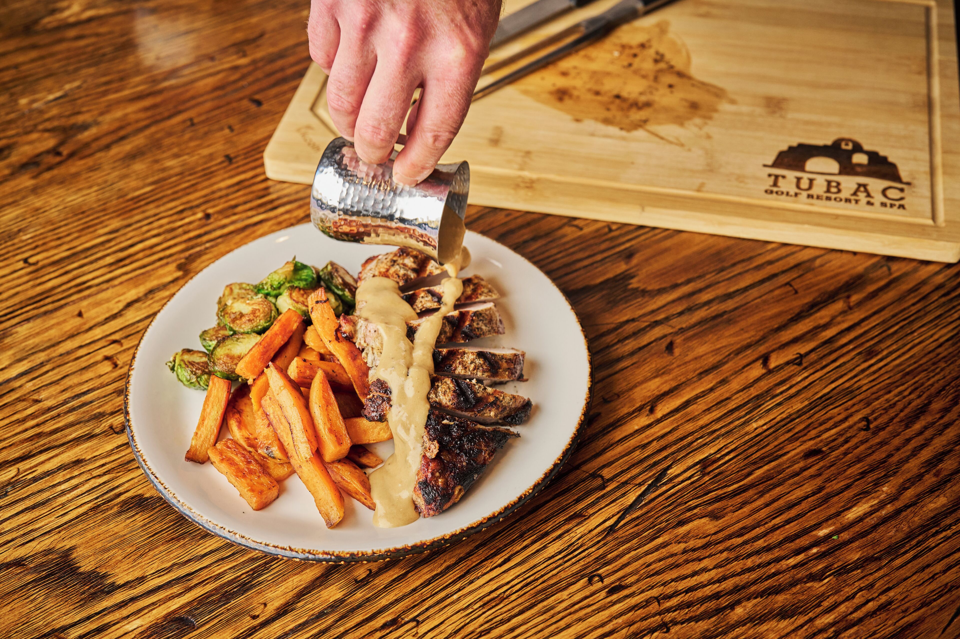 A plate of food with fries, meat, and vegetables, being garnished with a sauce.