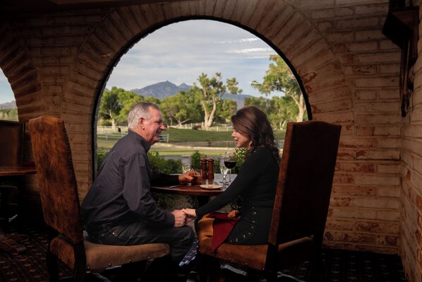 A couple dining at a table with a view of a golf course and mountains through an arched window. - Tubac Golf Resort & Spa (Tubac)