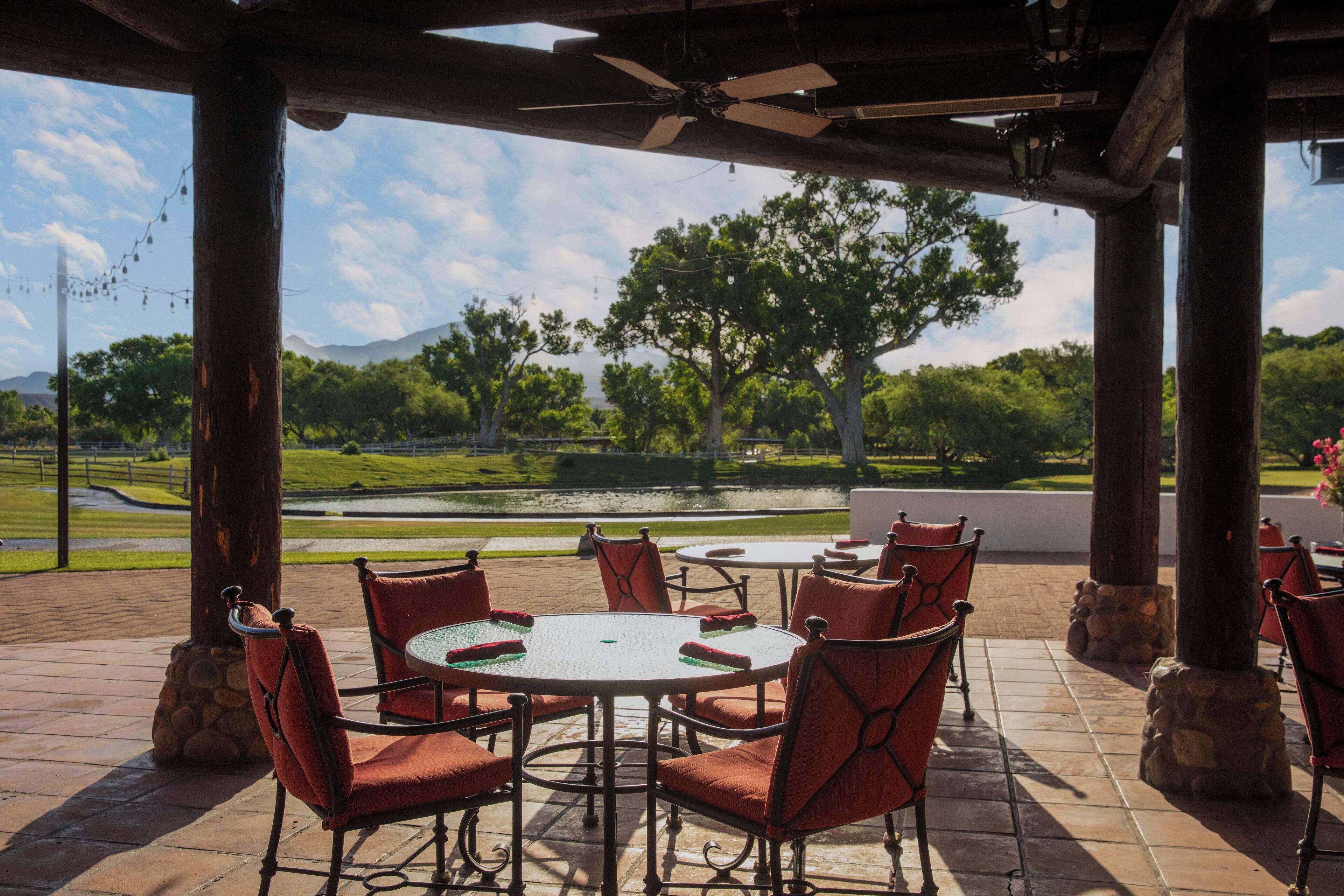 An outdoor patio with a round table and chairs, surrounded by stone pillars, overlooking a scenic landscape with trees and a body of water.