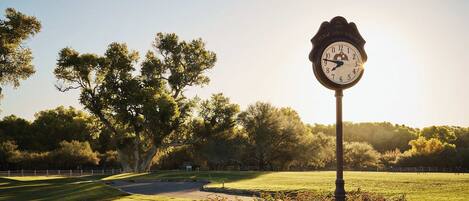A clock with "Tobacco Golf Resort" on it, set in a park with trees and a clear sky.