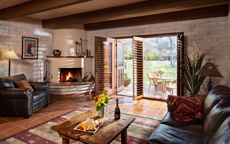 A cozy living room with a fireplace, leather sofas, a coffee table with snacks, and a view of the outdoors.