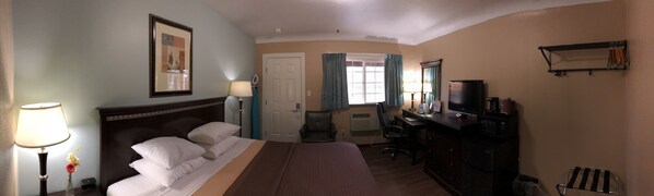 A hotel room with a bed, a desk, a television, and a window with curtains.
