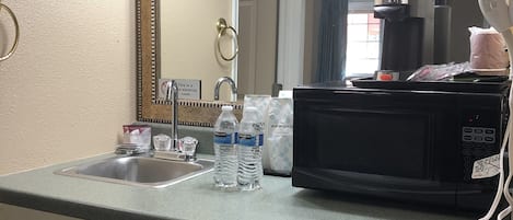 A hotel bathroom with a sink, a mirror, a hairdryer, and a microwave.