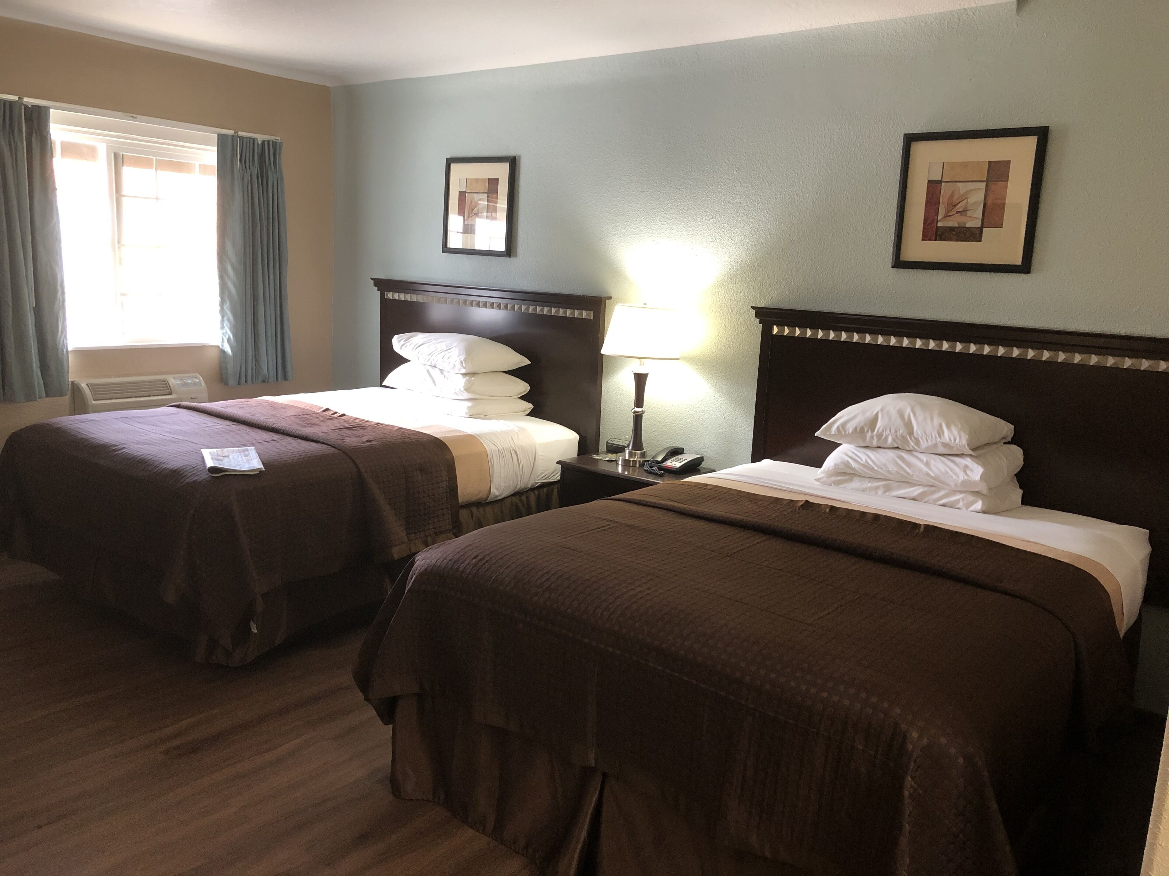 A hotel room with two beds, a bedside table with a lamp, a telephone, and a framed picture on the wall.