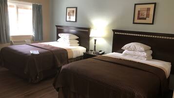 A hotel room with two beds, a bedside table with a lamp, a telephone, and a framed picture on the wall.