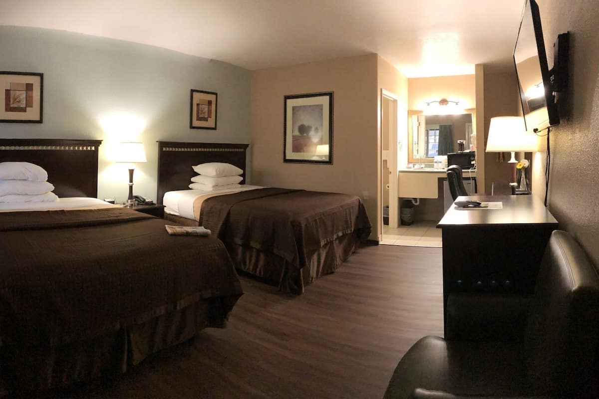 Une chambre d’hôtel avec deux lits, un bureau, une chaise, un miroir et un téléviseur.
