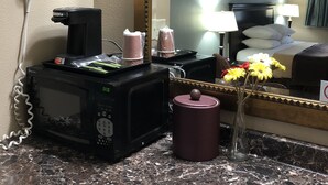 Ein Hotelzimmer mit Marmorplatte, einem Haartrockner, einer Mikrowelle, einer Kaffeemaschine, einer Vase mit Blumen und einem großen Spiegel, der das Zimmer reflektiert.