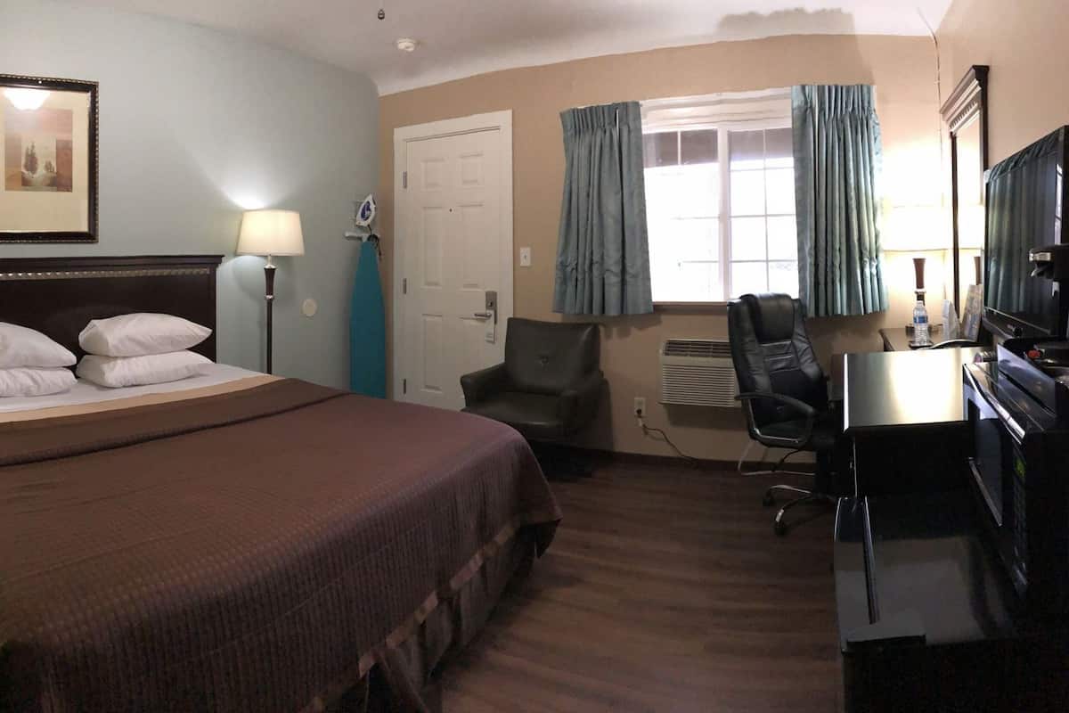 Une chambre d’hôtel comprenant un lit, des lampes de chevet, un bureau avec une chaise, une télévision et une porte.