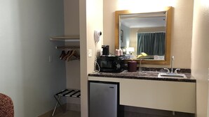 Eine kompakte Küche mit Mikrowelle, Kaffeemaschine und einem kleinen Kühlschrank. Ein Spülbecken mit Spiegel darüber und einem Kleiderhaken versehen. Handtuchhalter vorhanden.