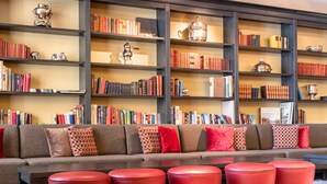 A library with a long sofa, red chairs, and bookshelves filled with books and decorative items. - Hotel Kaiserhof Kitzbuehel (Kitzbuhel)