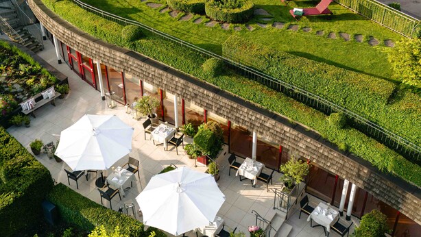 An outdoor terrace with seating, a garden, and a building with a sloped roof. - Hotel Kaiserhof Kitzbuehel (Kitzbuhel)