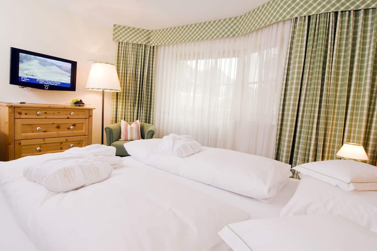 A hotel room with a TV on the wall, a wooden dresser, two beds with white linens, and green checkered curtains.