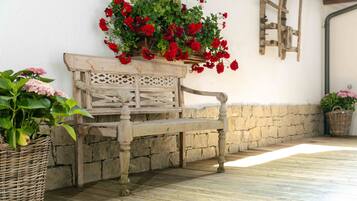Un banc en bois avec un panier en osier rempli de fleurs rouges, un mur de pierre et une structure de plafond en bois.