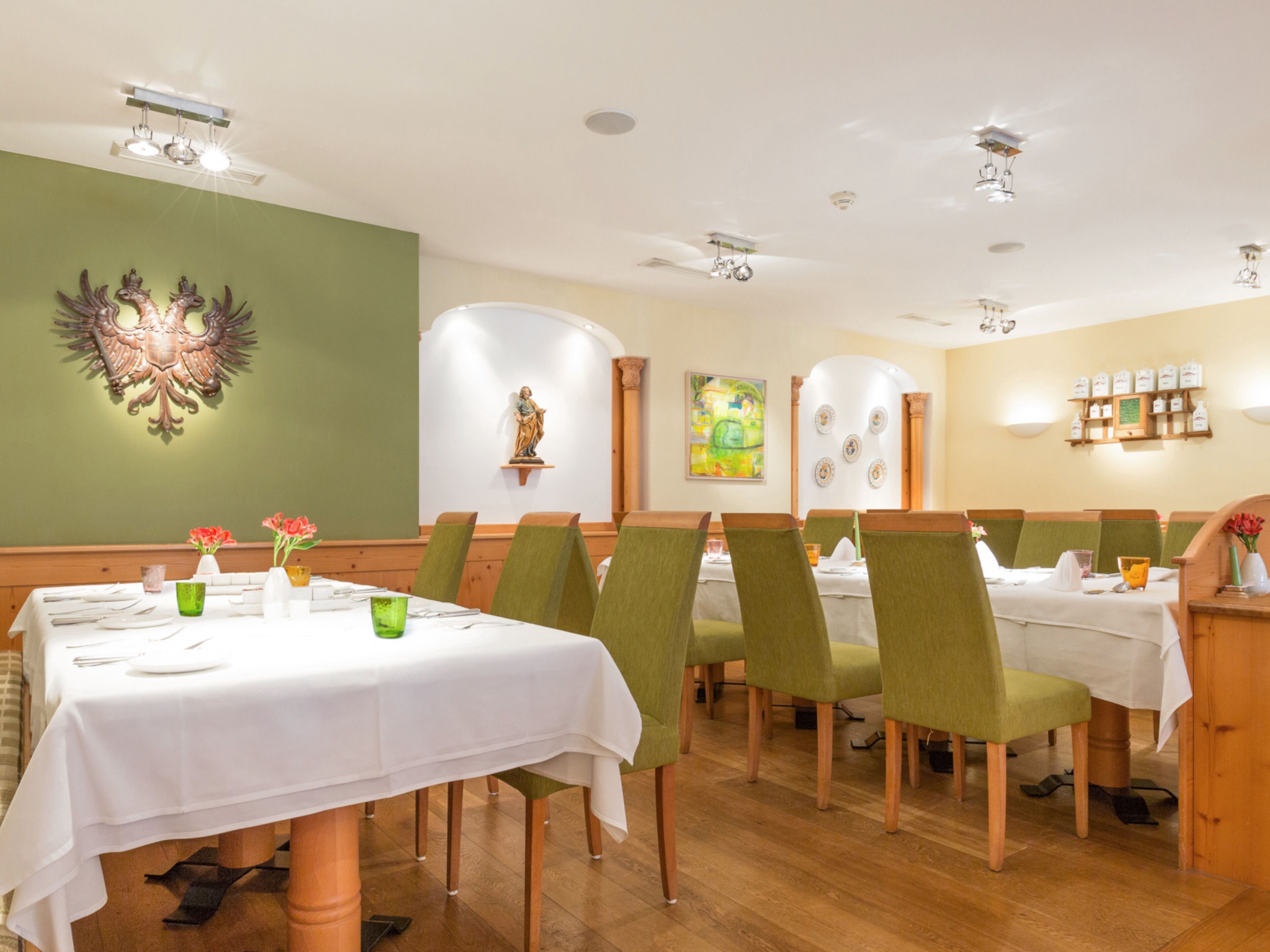 A restaurant with green chairs, white tablecloths, and a wooden floor.
