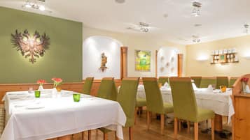A restaurant with green chairs, white tablecloths, and a wooden floor.