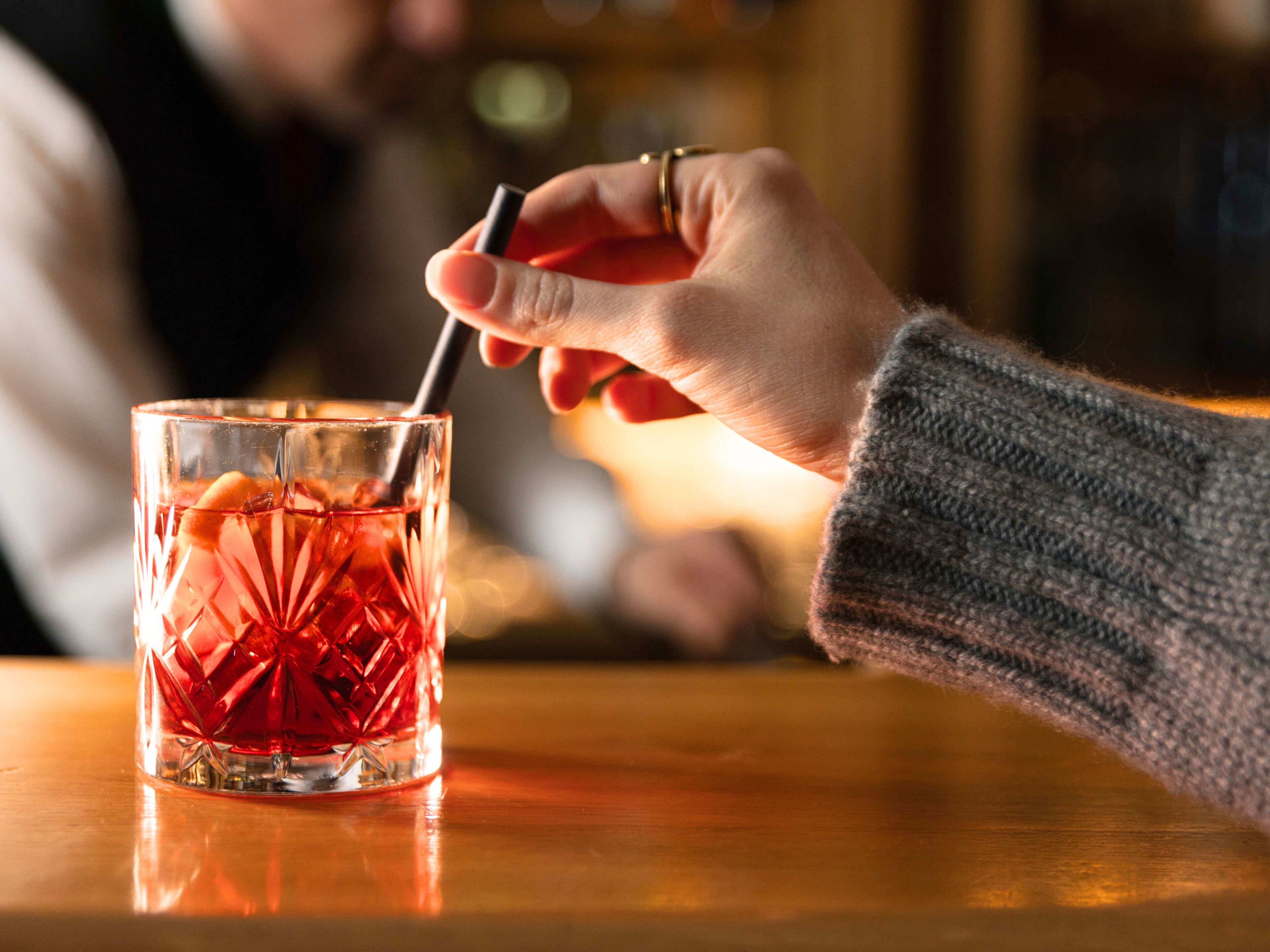 Eine Hand hält einen Strohhalm, ein Glas mit strukturierter Oberfläche und eine Holzfläche.