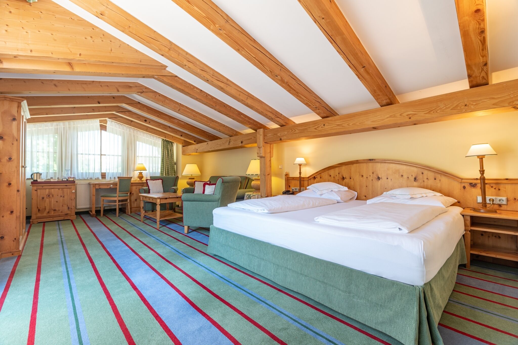 Een kamer met een bed, twee nachtkastjes, een bureau, een stoel en een raam met gordijnen.