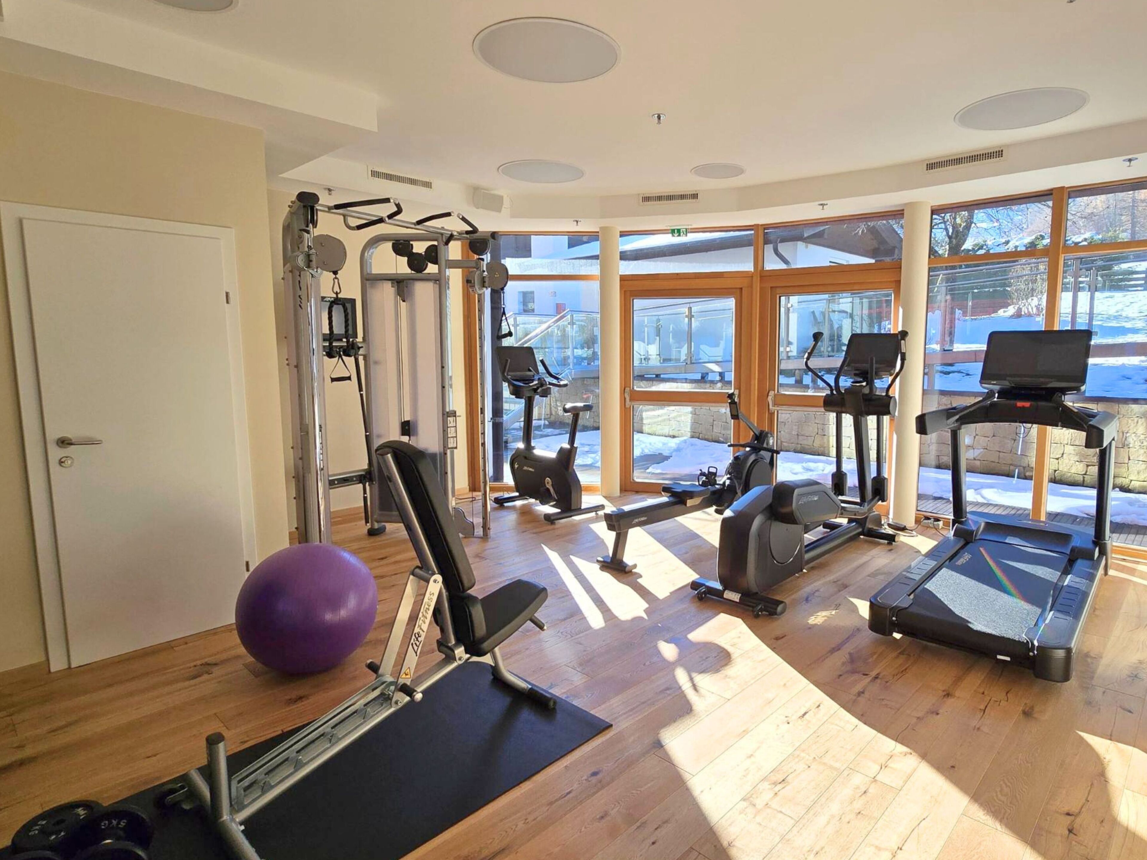 A gym with cardio machines, weight equipment, and large windows.