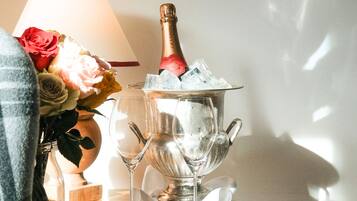 Una botella de champán en un cubo de hielo plateado con una copa y rosas sobre una mesa.