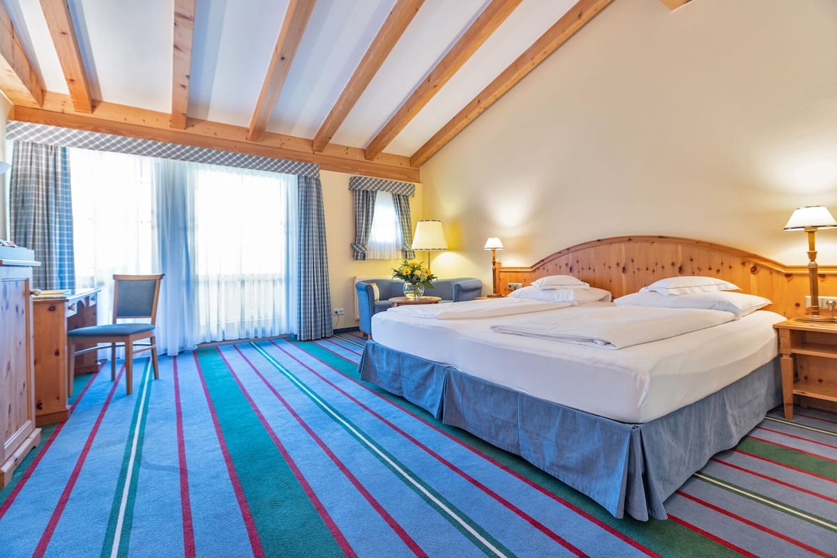 A hotel room with a large bed, a desk, a chair, and a window with curtains.
