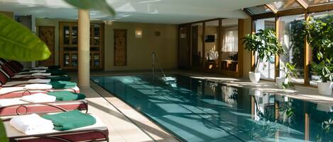An indoor swimming pool with lounge chairs and potted plants.