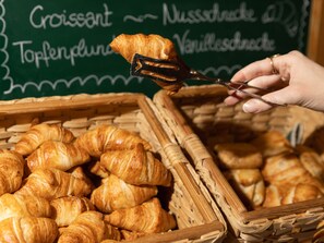 Kori täynnä croissantteja ja käsi, joka pitää haarukalla croissanttia.