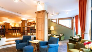 A hotel lobby with a wooden floor, blue armchairs, a wooden column, and a staircase. - Hotel Kaiserhof Kitzbuehel (Kitzbuhel)