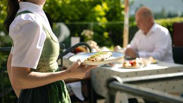 A woman in traditional attire holding a plate of food, standing at an outdoor table with a man seated.